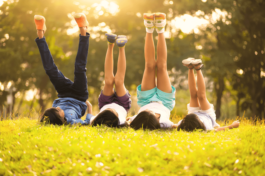 Four children lie on grass with legs in air.