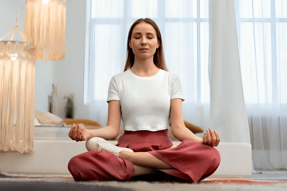 A woman meditating peacefully in a bright room with closed eyes.