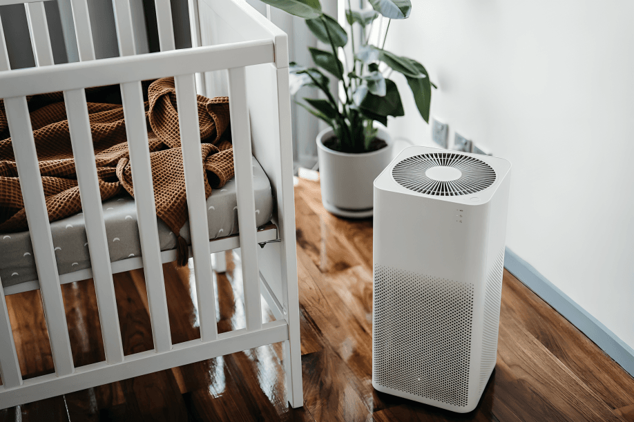 Air purifier next to crib and plant.