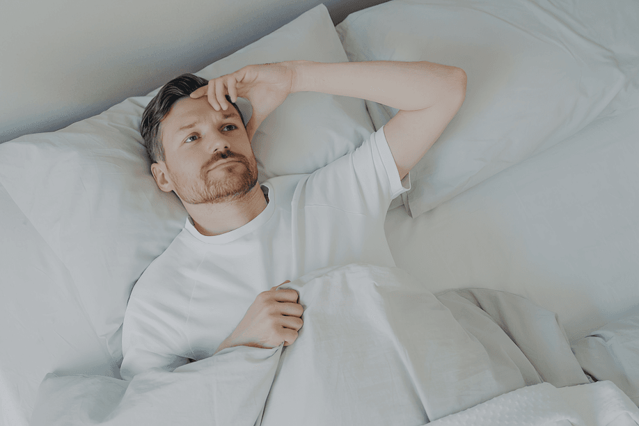 The man lies in bed, awake, with his hand on his forehead.