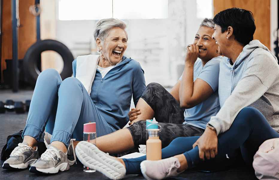 Three smiling women sitting and laughing in a gym.