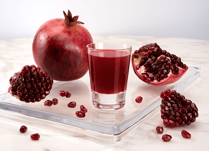 A glass of pomegranate juice with whole and cut pomegranates.