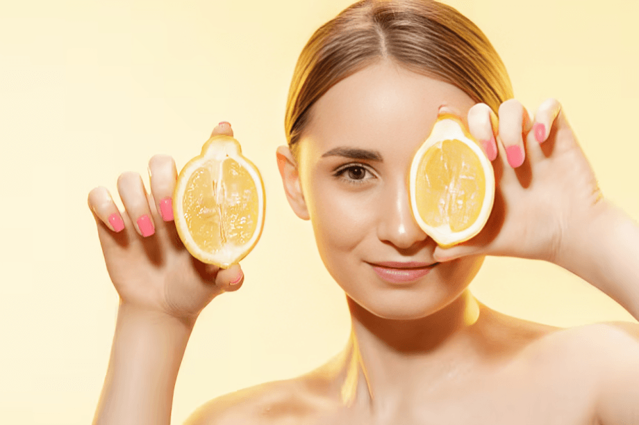 Smiling woman holding two lemon halves to her eyes.