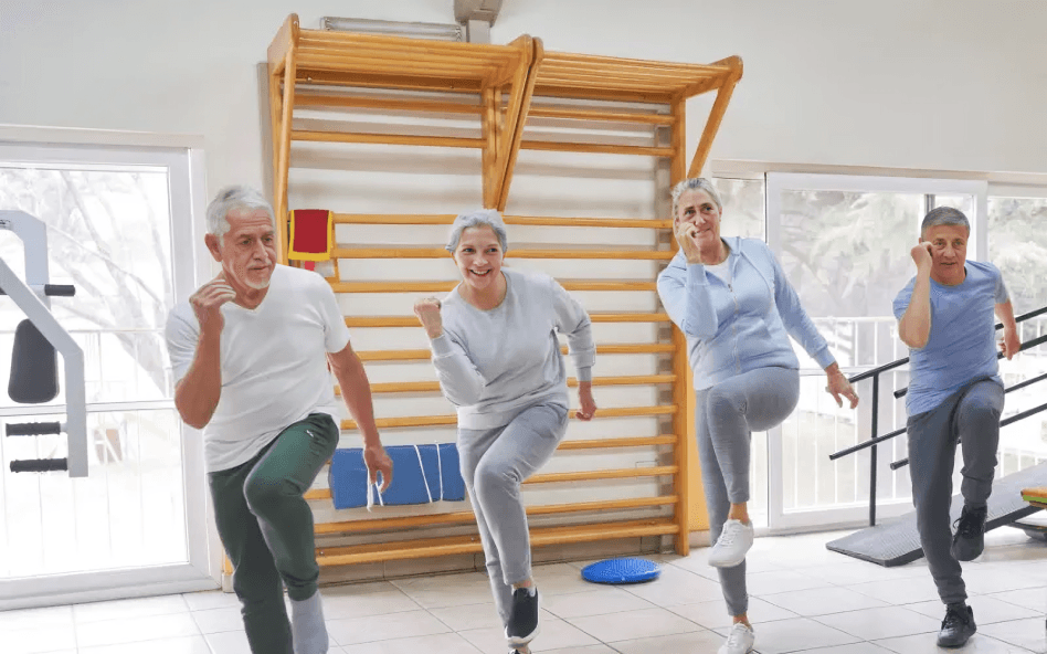 Happy seniors doing leg exercises in a gym.