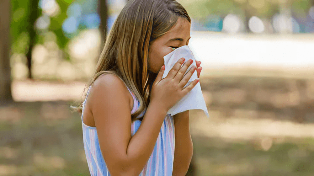 Girl with allergy wiping nose with tissue.
