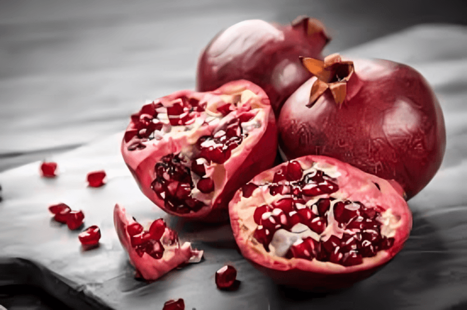 Several ripe pomegranates, some cut open, on a dark surface.