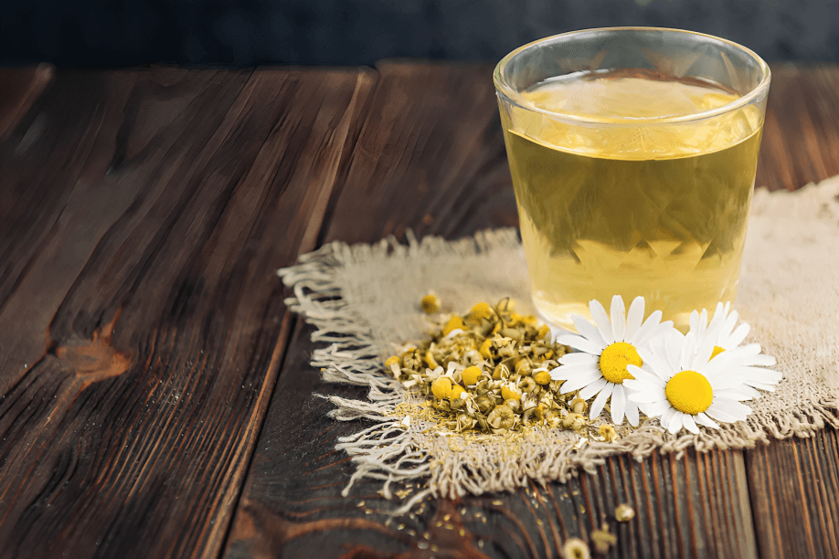 Chamomile tea, dried flowers, and fresh daisies on wood.