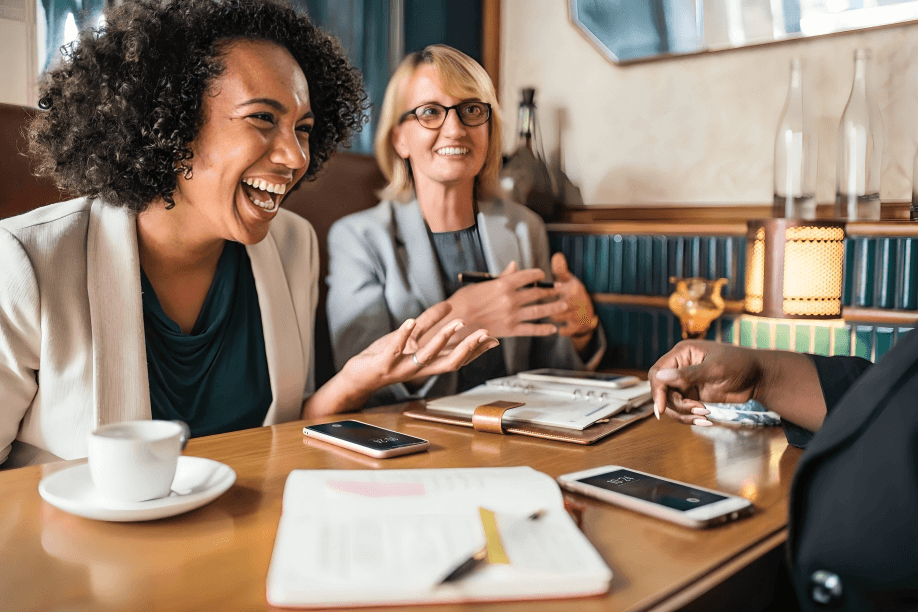 Three diverse women laughing and talking at a table.