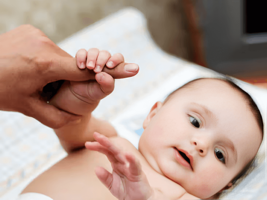 Baby grasps an adult's finger, looking upwards.