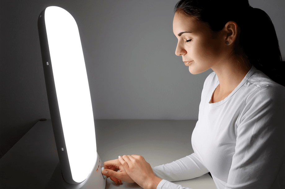 Woman using light therapy lamp for treatment.