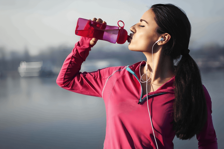 Woman in pink sportswear drinking water from a bottle.