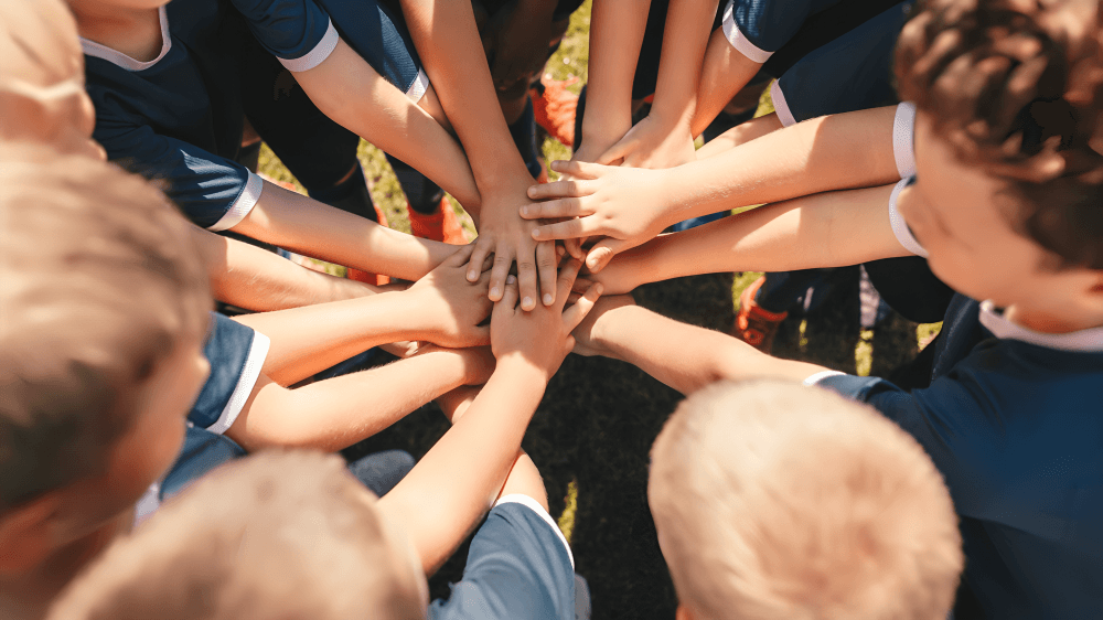 Youth soccer team with hands stacked in center, viewed from above.