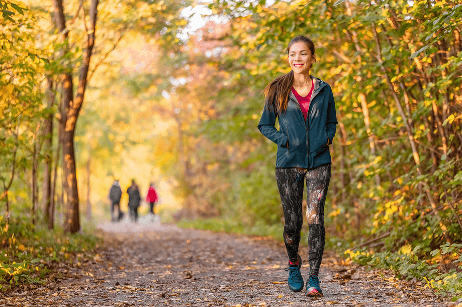 Woman jogging in a park with fall foliage.