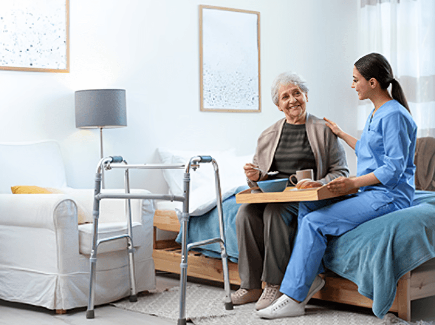 The caregiver brings a meal to the smiling senior woman.