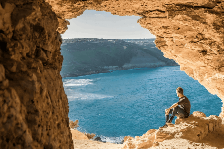 Person sits in cave overlooking ocean view.