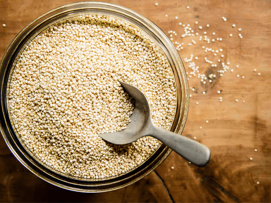 A bowl of quinoa with a scoop on wood.