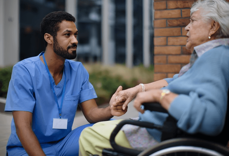A caregiver holds the hand of a senior woman in a wheelchair.
