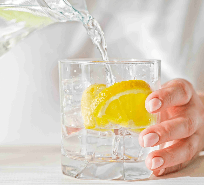 Water pouring into glass with ice and lemon.