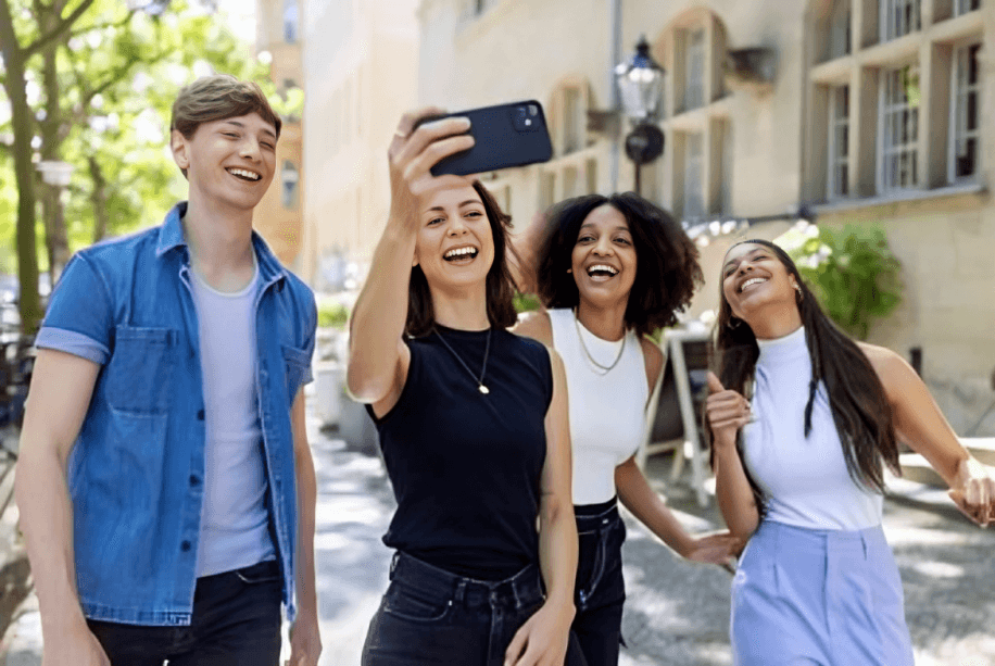 Four diverse friends taking a selfie outdoors, laughing cheerfully.