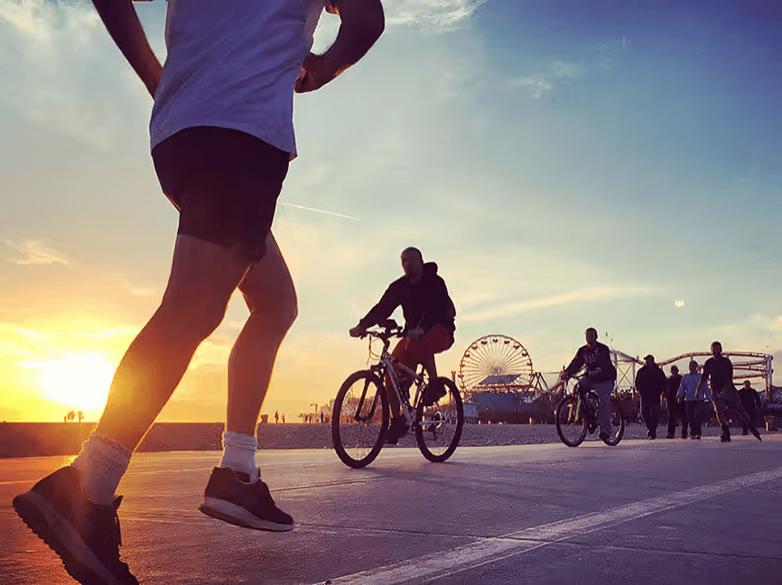 People jogging and biking at sunset by the pier.