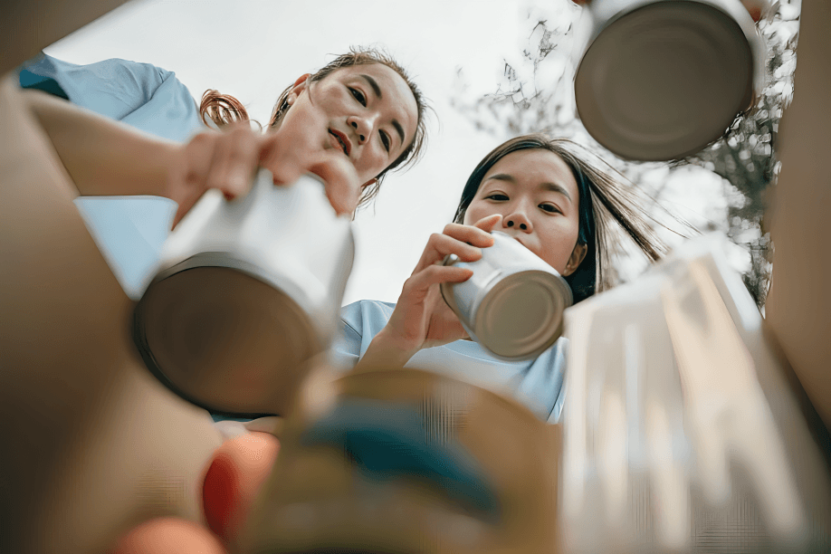 Two people, possibly East Asian, recycling cans into a bin.