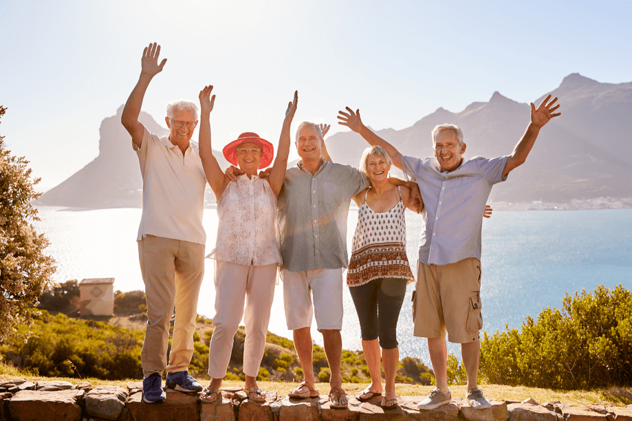 Jubilant seniors waving by a scenic waterfront.