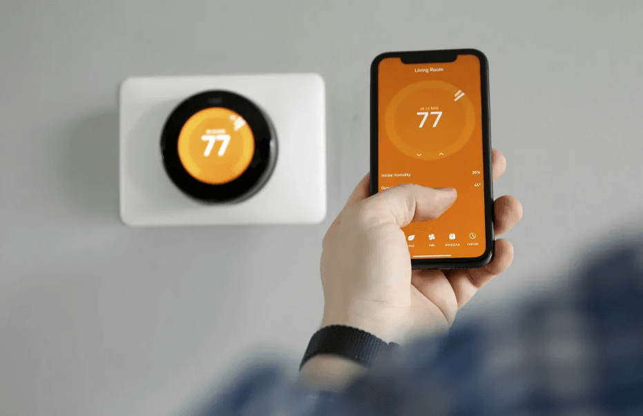 Man holding smartphone controlling smart thermostat.