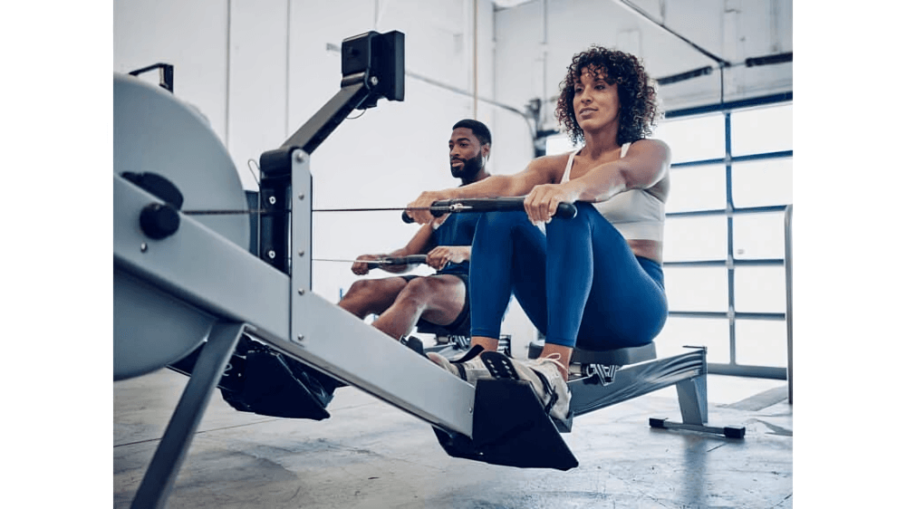 Two people exercising on rowing machines in a gym.
