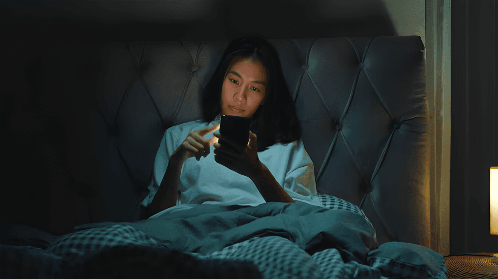 A woman looking at her mobile phone in her bed.