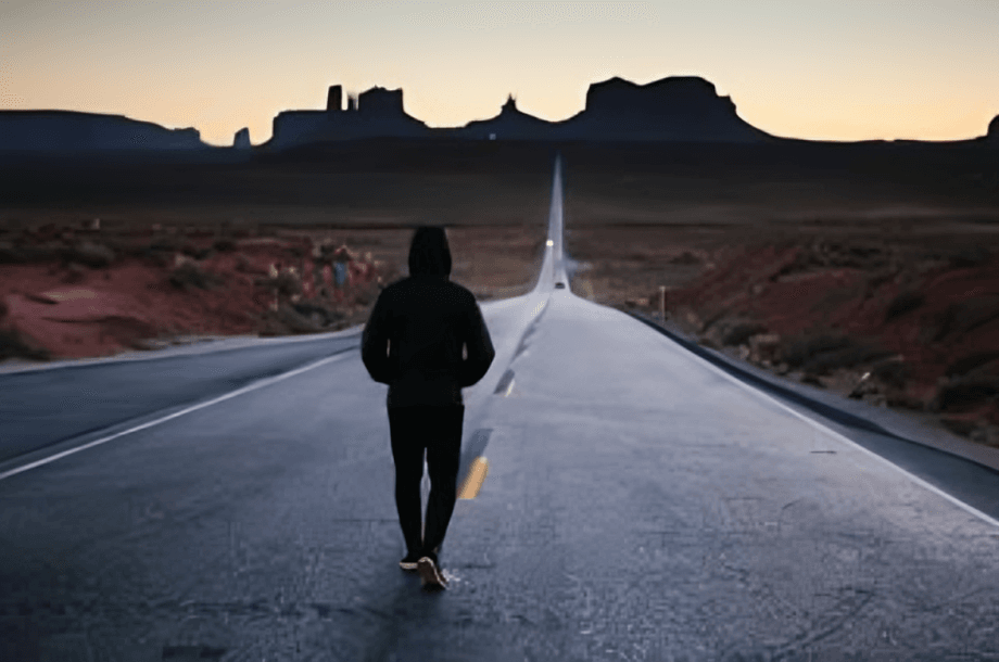A person walks on the road towards the distant landscape.