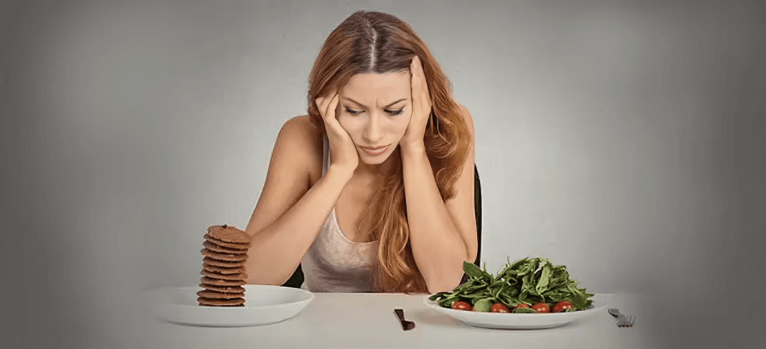 A woman choosing between a healthy salad and cookies.