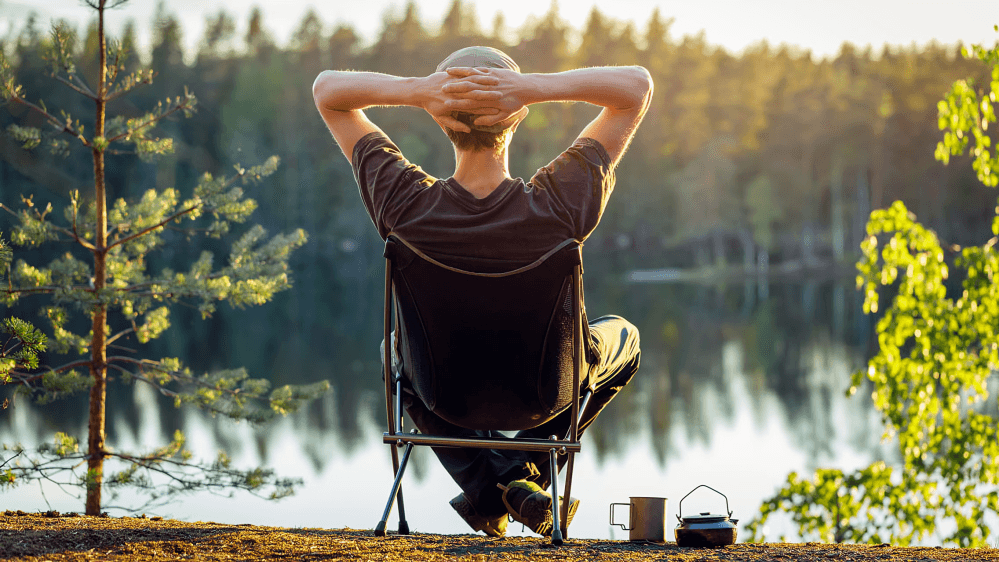 Person relaxing in chair by lake with arms up.