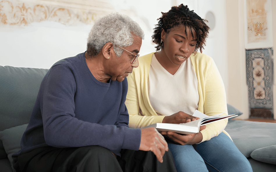 A caretaker and senior man reading a book.