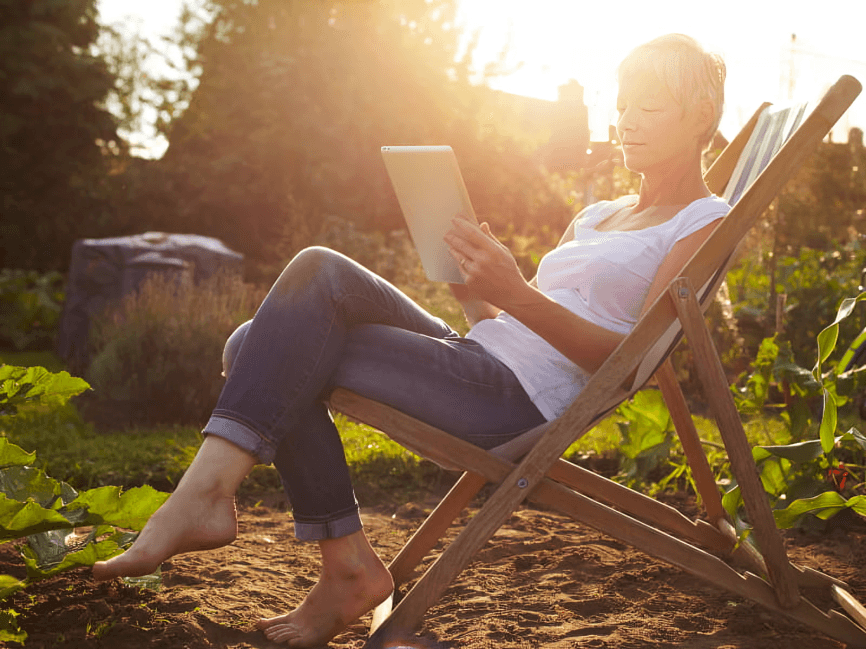 A woman reads on a tablet in sunshine.