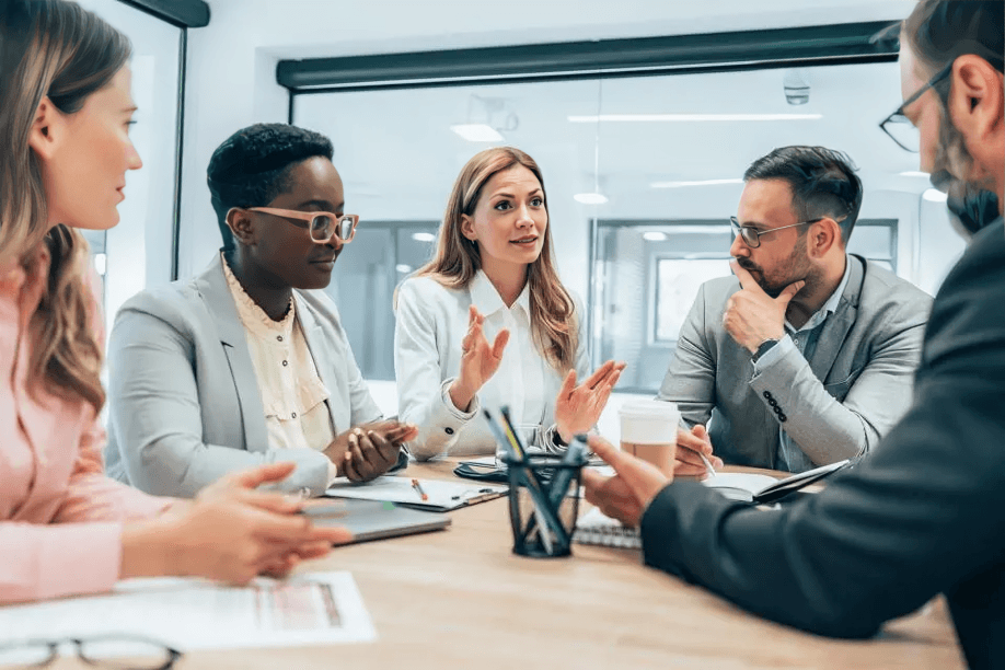 Five professionals engage in a discussion around a conference table.