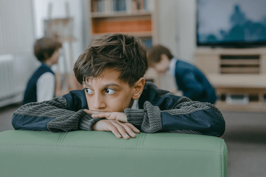 A young boy looks worried, with other children blurred.