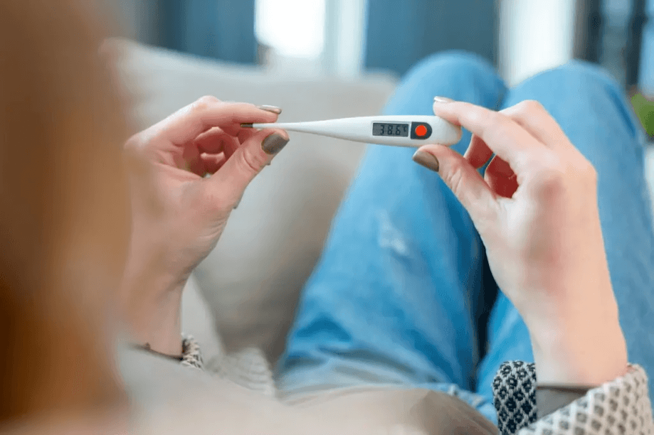 Woman holds a thermometer showing a high body temperature.