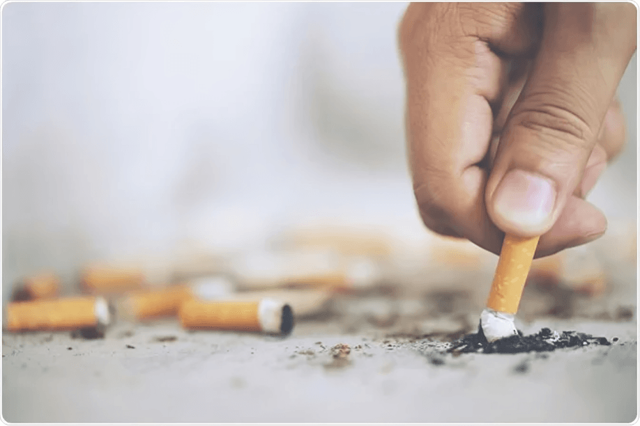 Hand extinguishing a cigarette butt on a dirty surface.