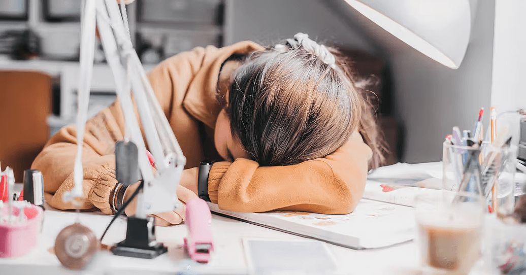 Person asleep on desk surrounded by study materials.