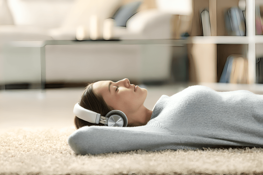A woman with headphones peacefully lies on a carpeted floor.