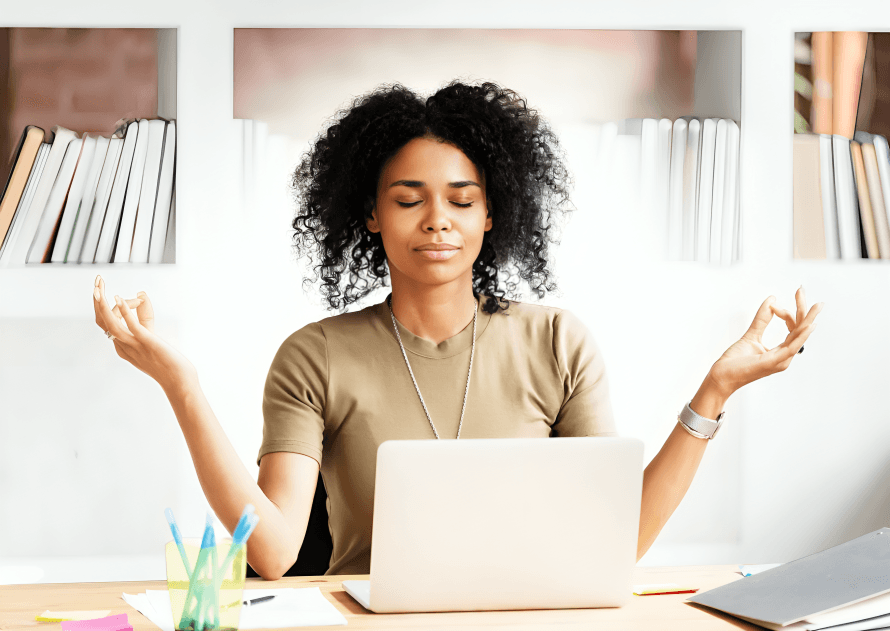 A woman with curly hair meditates at her desk.