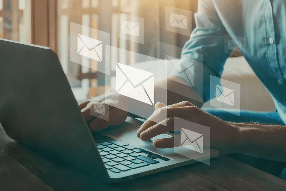 Hands typing on a laptop with floating email icons.