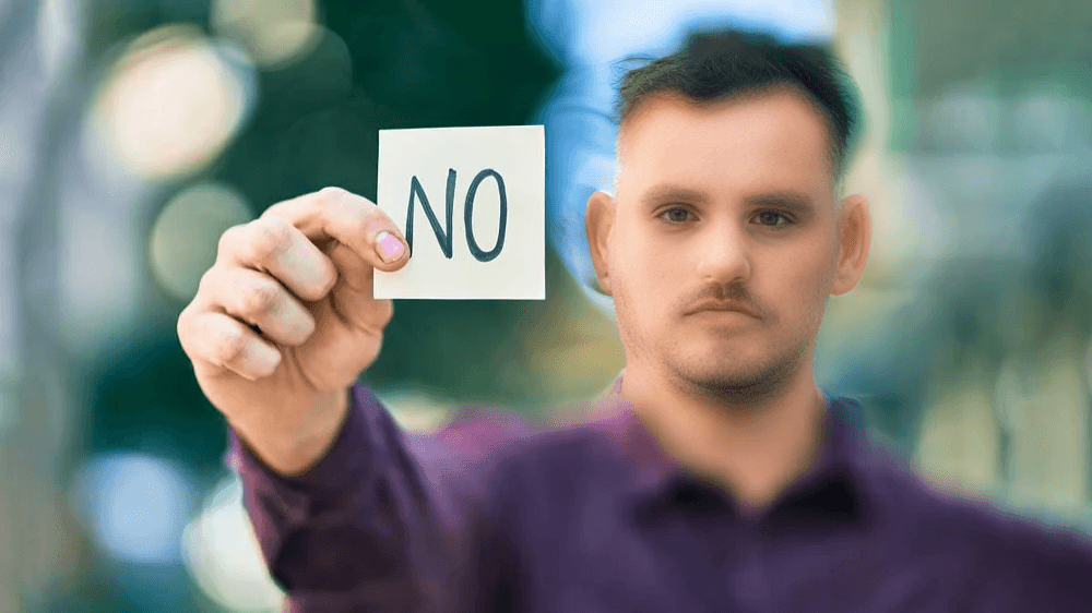 The man holds up a "NO" sign directly at the viewer.