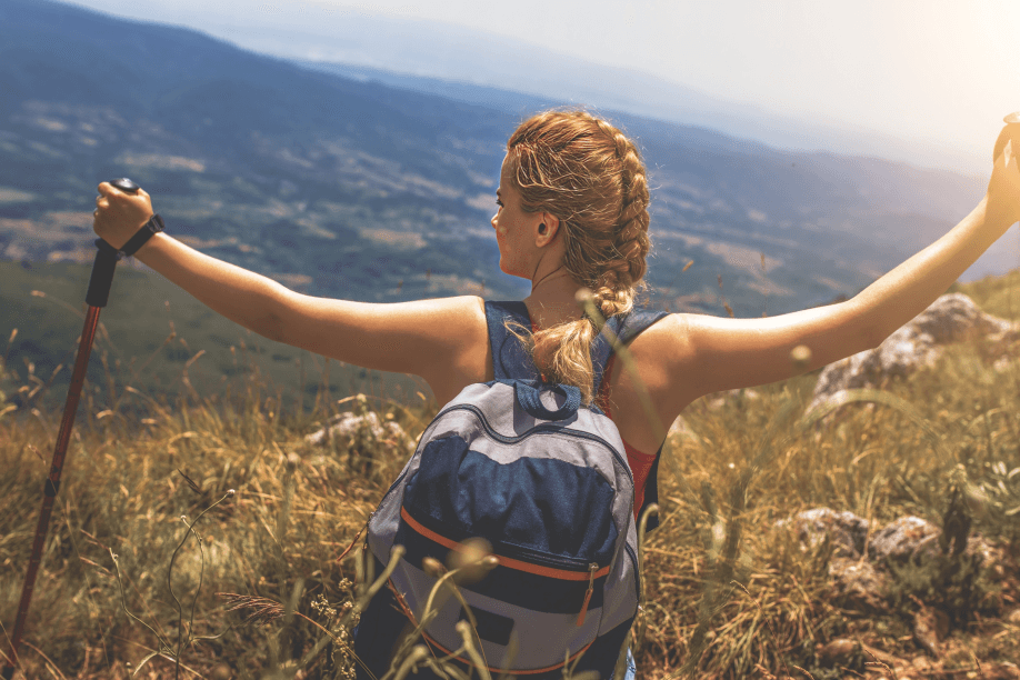 Woman hiker with backpack enjoying mountain view, arms outstretched.