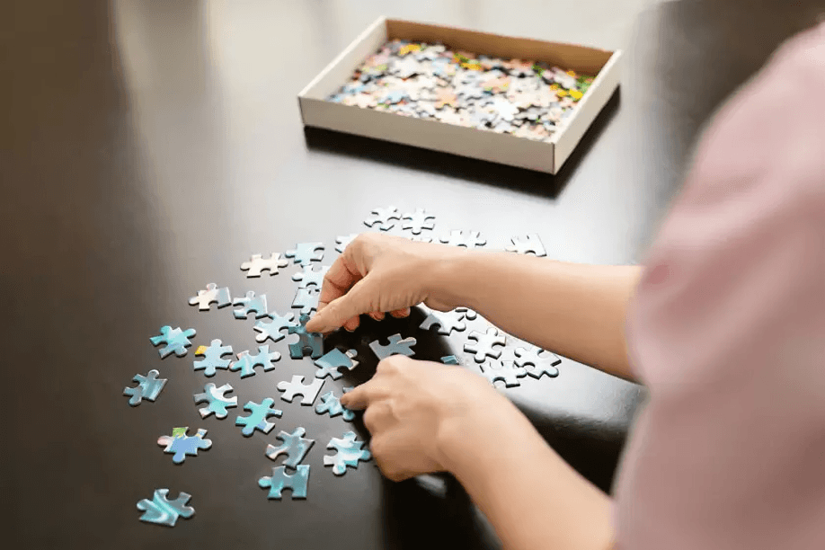 Hands assembling a jigsaw puzzle on a table.