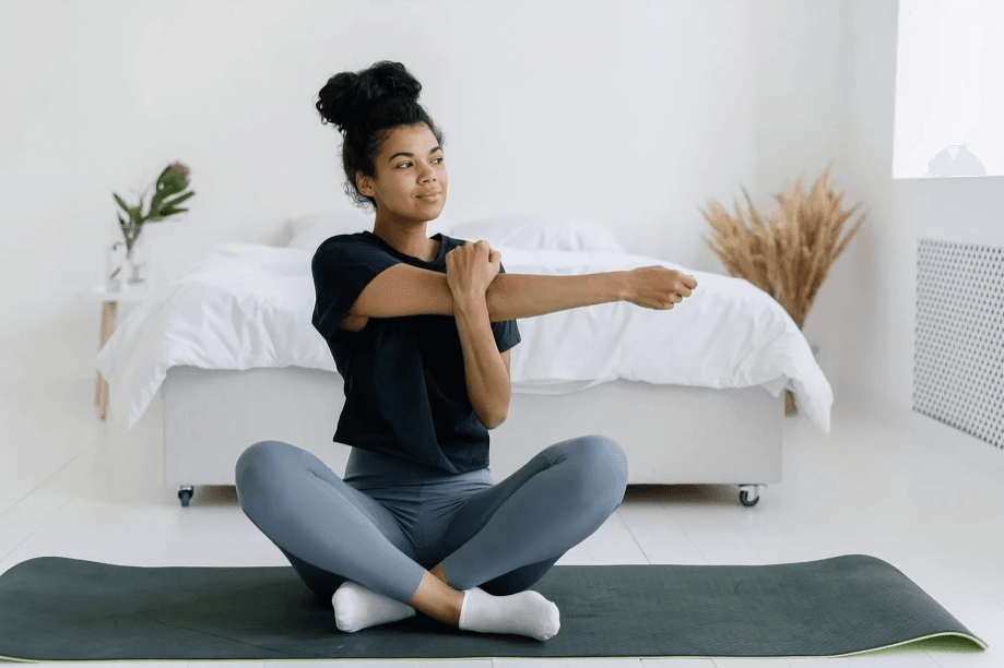 Woman with dark skin stretching arms on yoga mat.