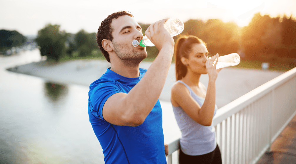 A man and a woman drinking water after exercising outdoors.