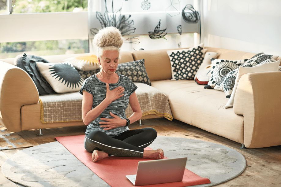 A person meditating on a yoga mat with a laptop.