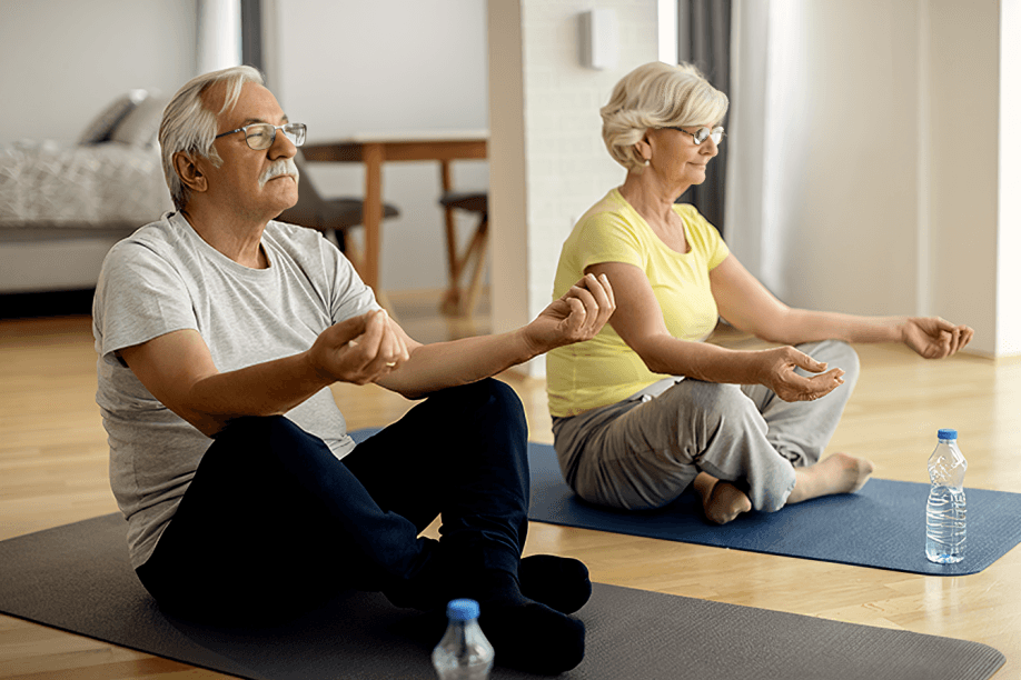 Two seniors meditating on yoga mats indoors.