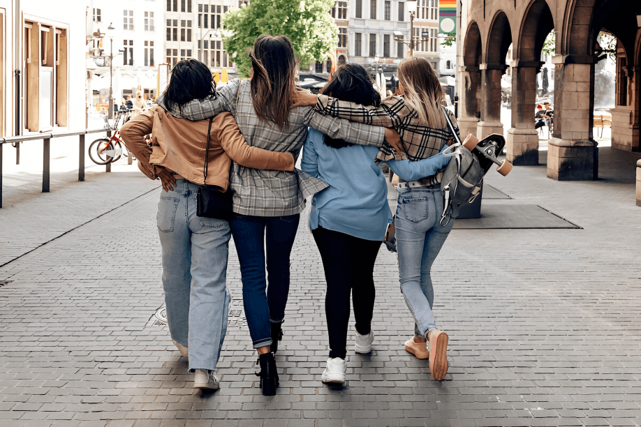 Four young women with arms around each other walking.